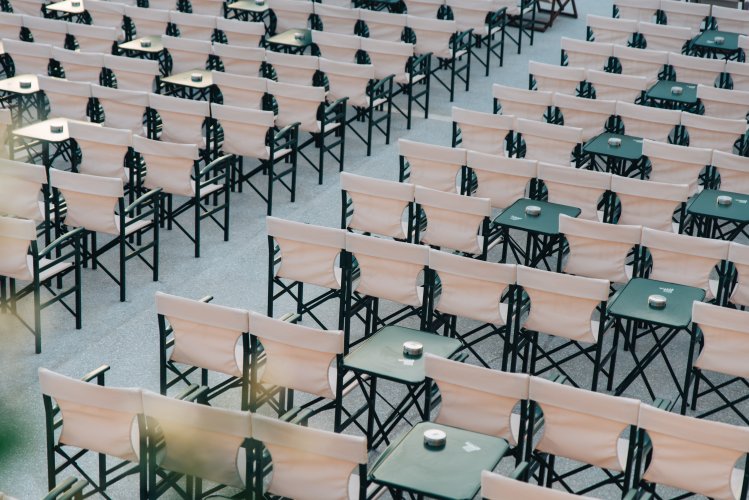 rows of white folding chairs with green tables attached, set up in an outdoor venue.
