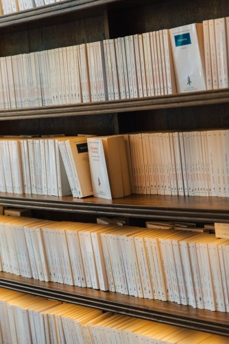 Neatly aligned books with cream-colored covers displayed on a wooden shelf.