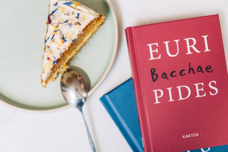 A slice of cake topped with edible flowers on a plate, next to a red book with bold white text.