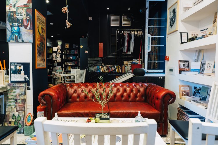 A cozy bookstore café interior featuring a red leather couch, a white coffee table, and bookshelves filled with books and decorations.