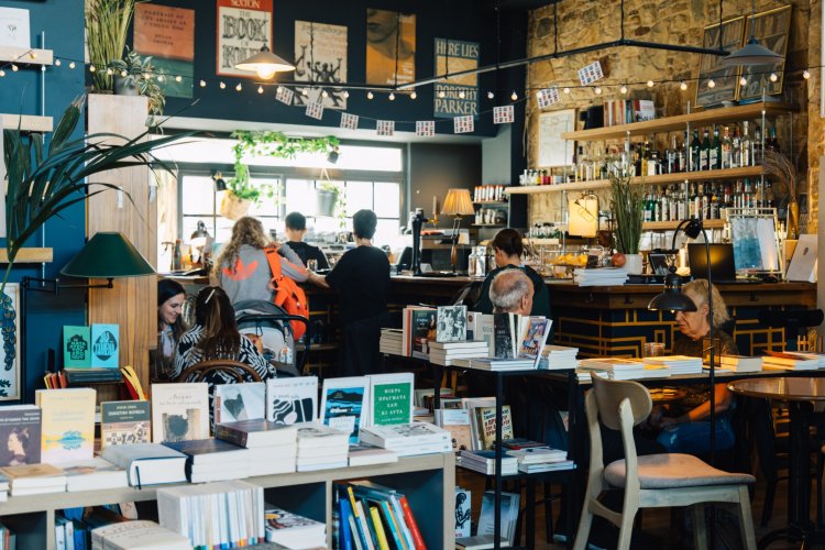 Interior of a lively café within a bookstore, with patrons reading, chatting, and browsing shelves filled with books under warm lighting.