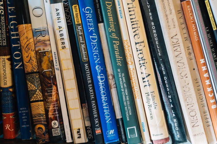 A close-up of a row of books on a shelf, featuring titles on topics like Greek design, erotic art, and mythology, with vibrant covers arranged neatly.