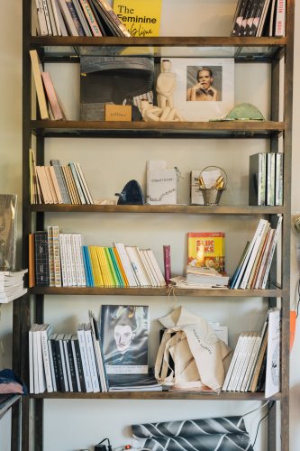 A wall-mounted shelf holding a collection of art and design books along with decorative items, including small sculptures and an art print.