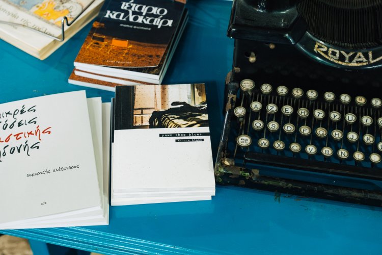 Close-up of a vintage typewriter with stacks of books in Greek on a vibrant blue table.