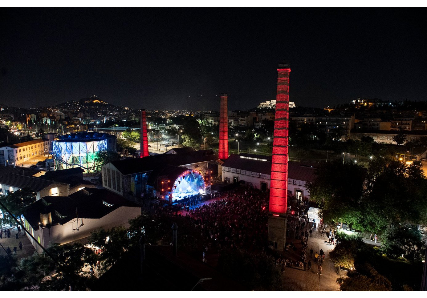 nighttime drone view of a city, crowd gathered at a concert at an industrial space