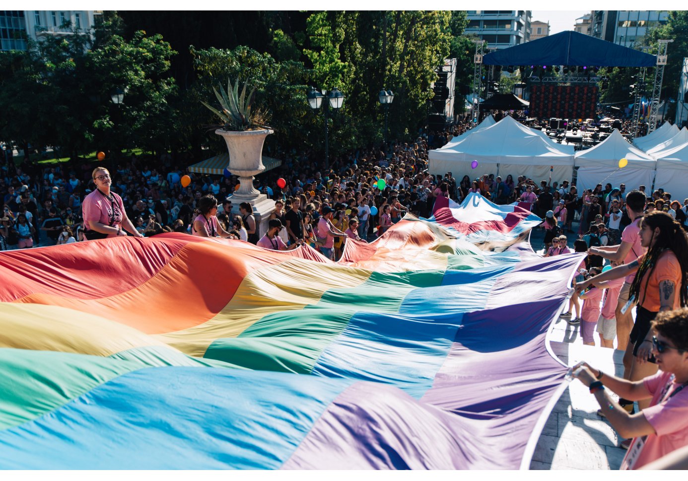 people holding a rainbow flag, crowds gathered in square