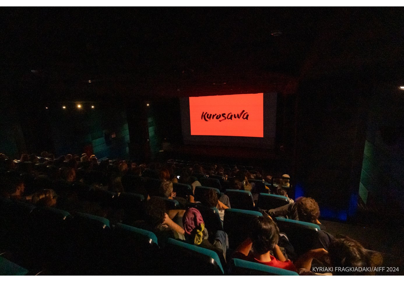 people watching a movie, on the screen there is lettering that reads "Kurosava"