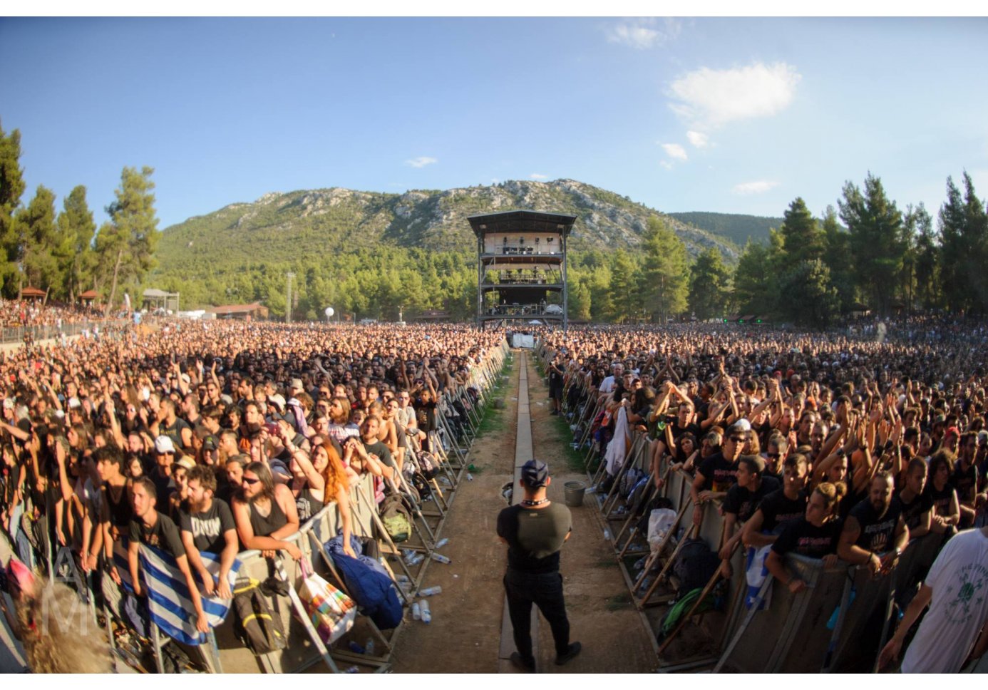 A security man stands among the crowd in an outdoor concert venue.